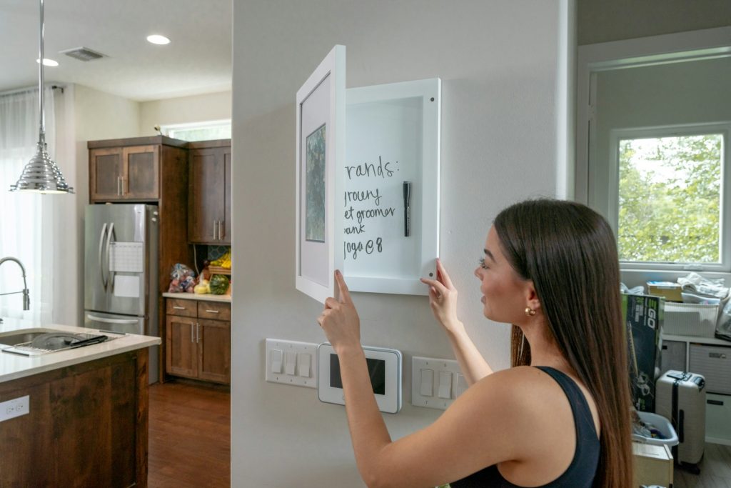 Woman opens wall cabinet with whiteboard in kitchen displaying errands like grocery shopping and yoga appointment