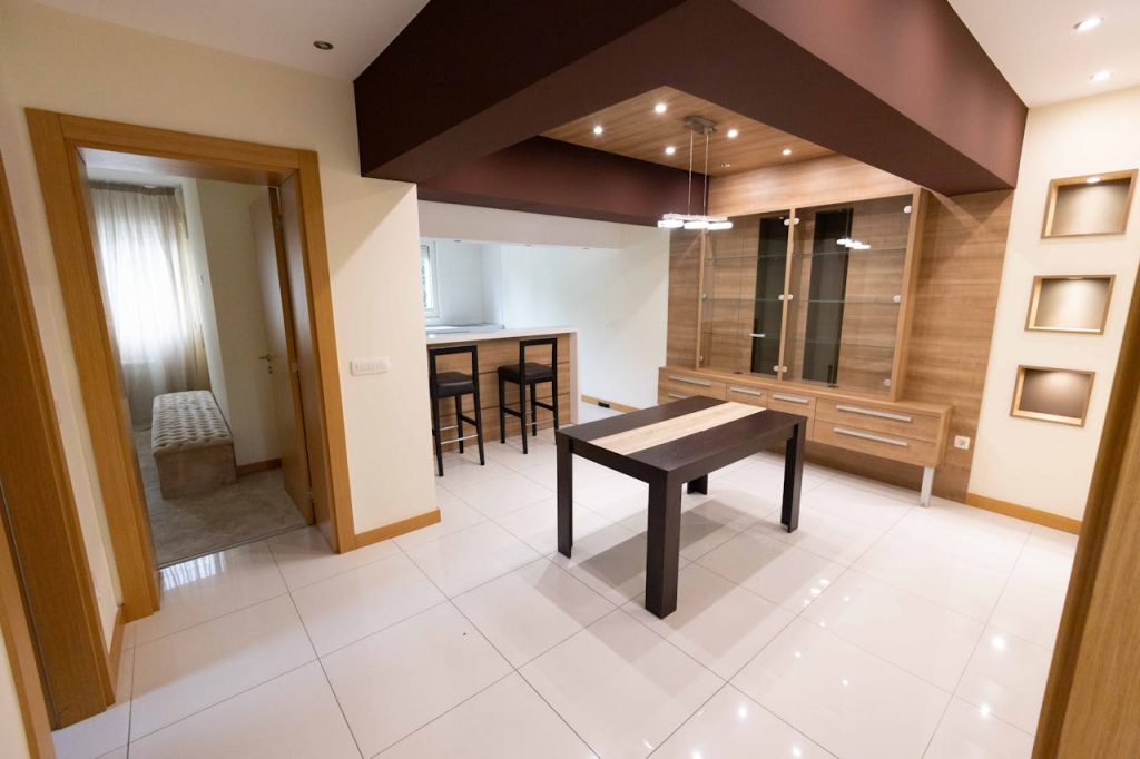 Modern dining room with wooden furniture, tiled floor, and a small bar area with stools in a well-lit space