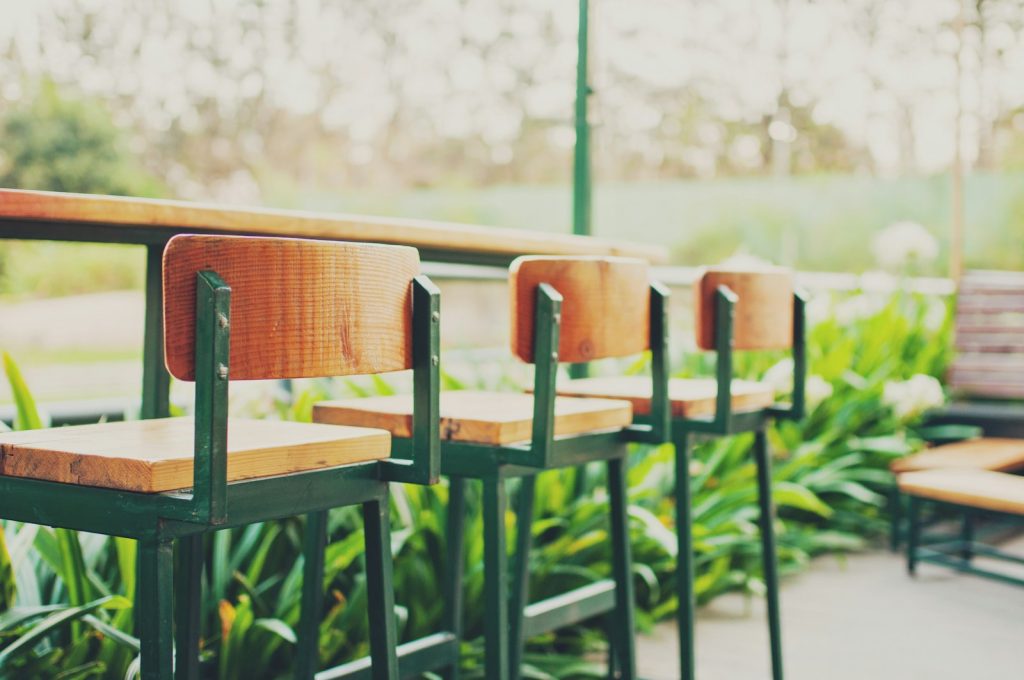 Wooden bar stools outdoors with green plants in the background, creating a serene and inviting atmosphere